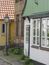 Half-timbered house with white windows and green wood panelling, next to it a street lamp and