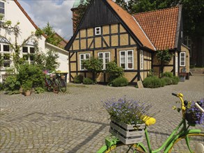 Charming village square with half-timbered house, colourful flowers and parked bicycles under a