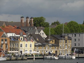 Town view with historic buildings, chimneys and boats on the waterfront under a cloudy sky,