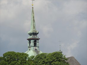 Detail of a church tower in front of a cloudy sky with green trees in the foreground, Kappeln,