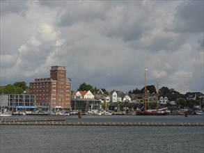 Buildings and boats along a coastline under a cloudy sky, Kappeln, Schleswig-Holstein, Germany,