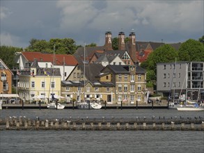 Coastal town with many buildings and boats on the water, under a partly cloudy sky, Kappeln,