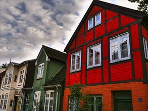 Cornice decorated half-timbered houses in red and green under a cloudy sky, Eckernförde,