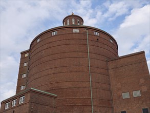 A massive brick building with a round dome rises into the sky on a cloudy day, Kappeln,