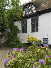 Historic building with white walls and blooming flowers, surrounded by green plants, Arnis,