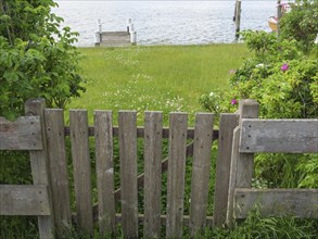 Wooden fence leading to a meadow and a body of water, surrounded by trees and flowers, Arnis,