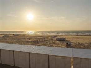 A peaceful sunset on the beach with huts in the foreground and the sea in the background, de haan,