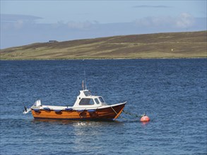 An orange-coloured boat floats on the calm sea, attached to a red buoy, Lerwick, Shetlands,