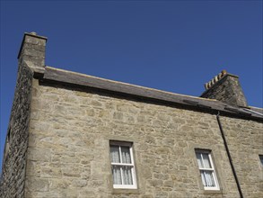 Close-up of a traditional stone house with two fireplaces under a clear blue sky, Lerwick,