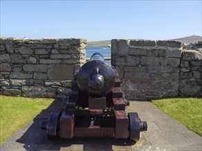 An old cannon pointing to the blue waters of the coast in front of a historic wall and standing on