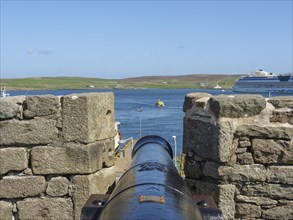 View along the wall of an old fortification with a cannon pointing to the sea and a ship, Lerwick,