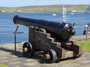 A historic cannon aimed at the calm blue sea on a clear sunny day, Lerwick, Shetland, Scotland,