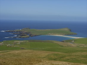 Elevated perspective of an island with a coastline surrounded by green grass and a sandy beach,