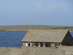 Small house with brown roof and red shutters set against a tranquil coastal landscape, Lerwick,