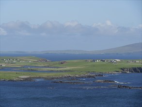 Green island with extensive coastline, surrounded by sea and under a cloudy sky, Lerwick,