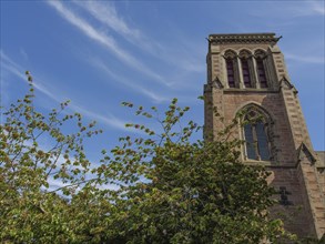 The gothic tower of a church in front of a sky with clouds and surrounded by trees, inverness,