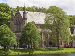 A large historic church surrounded by lush green trees, next to a tranquil river, inverness,