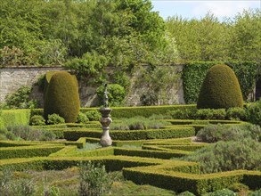 A manicured garden with symmetrical hedges and a centrally placed sculpture in a green landscape,