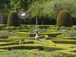 A formal garden with symmetrically trimmed hedges and a central sculpture, all set in a verdant