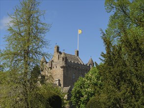 A historic castle with a waving flag on the tower, surrounded by green trees, inverness, Scotland,