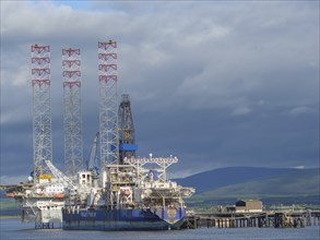 Industrial plant with an oil drilling platform in the harbour, surrounded by water and mountains in