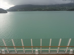 View of calm, greenish water and surrounding misty mountains, seen from a boat, eidfjord, norway