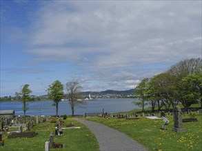 Cemetery with gravestones and trees, in the distance a lake and cloudy sky, Haugesund, norway