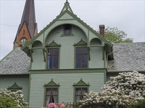 Green wooden house with pointed roof and decorative ornaments in front of a church, Haugesund,