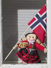 A doll in traditional traditional costume holds a Norwegian flag and stands in a window, Stavanger,