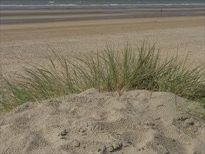 View from the sand hill onto the vast, empty beach with the sea in the background and a clear sky,