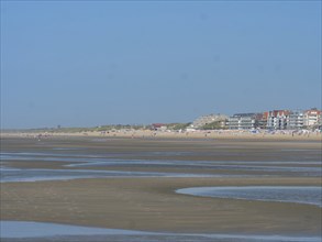 Sandy beach beach at low tide with calm sea and houses in the background under a clear blue sky, de