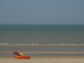 Beach with a colourful parasol and an orange and yellow striped deckchair in front of calm sea and