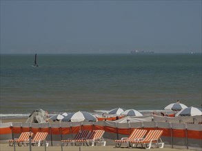 Beach full of orange and white deckchairs and parasols, a sailing boat on the sea and a blue sky,