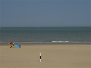 A quiet beach with a small tent in the sand, the sea in the background and a blue sky above, de