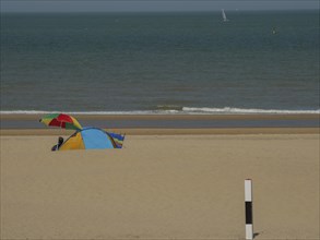 Colourful tent and parasol on a sandy beach, with calm sea in the background on a sunny day, de