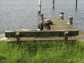 Dilapidated wooden bench at the end of a wooden footbridge leading into the water of a calm lake,