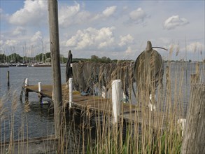 An old jetty on the lake with folded fishing nets, boats and clouds in the sky in the background,