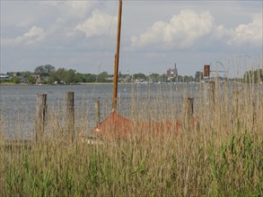 View through reed grass to a lake with boat, poles and cloudy sky, Arnis, Schleswig-Holstein,