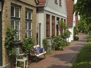 Terraced houses with red tiled roofs, green vegetation and a bench on a cobbled street, Arnis,