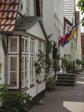 Simple residential buildings with floral decorations and a flag along a cobbled street, Kappeln,