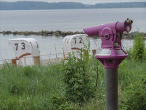 Purple binoculars with a view of numbered beach chairs and the calm sea, Eckernförde,