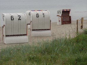 Several white beach chairs with numbers stand in front of a calm sea on a sandy beach, Eckernförde,