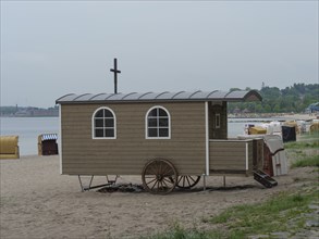 Wooden wagon with windows and cross on a beach, surrounded by beach chairs, Eckernförde,