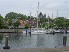 Yachts and sailboats in the harbour against a background of trees and buildings under a cloudy sky,