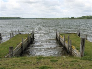 View of two harbour jetties with grass and wooden piles protruding into the water, Maasholm,