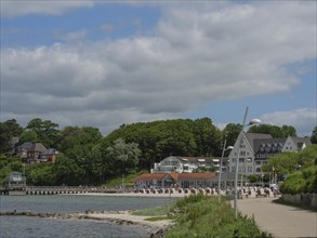 A coastal landscape with a promenade, small houses and green areas under a slightly cloudy sky,