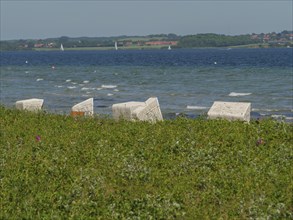 White beach chairs on the beach against the backdrop of waves and a green meadow, Flensburg,