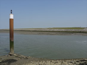 A coastal scene with a post in the water and a rocky shore under a clear sky, Hallig Hooge,