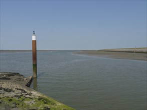 A coastal scene with a single post in calm water with clear sky and rocky shore, Hallig Hooge,