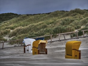 Various beach chairs in front of a grassy dune under a gloomy sky, juist, east frisia, germany